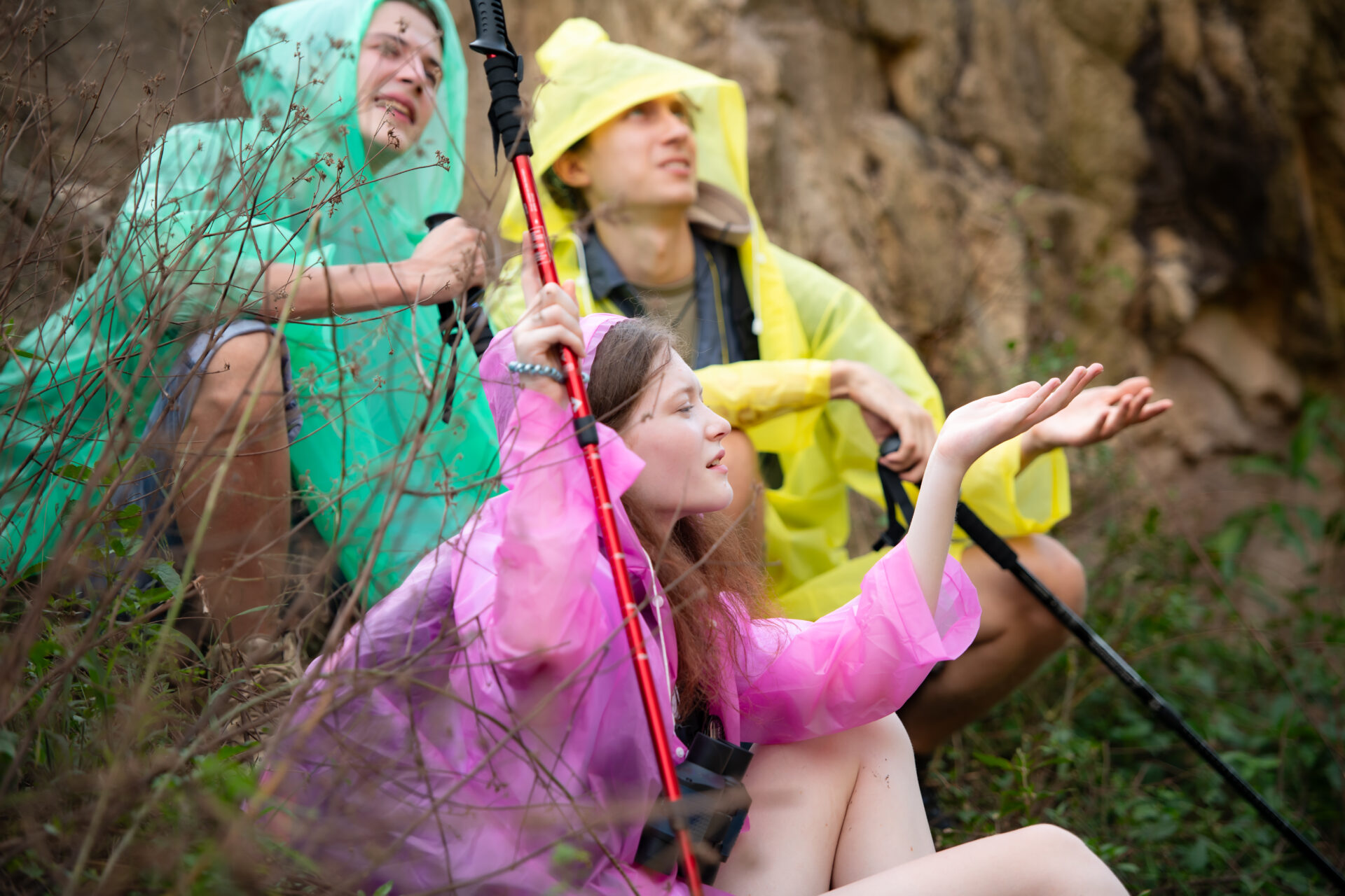 Group of friends in raincoat with backpacks hiking in the forest, Sit and shelter from the rain